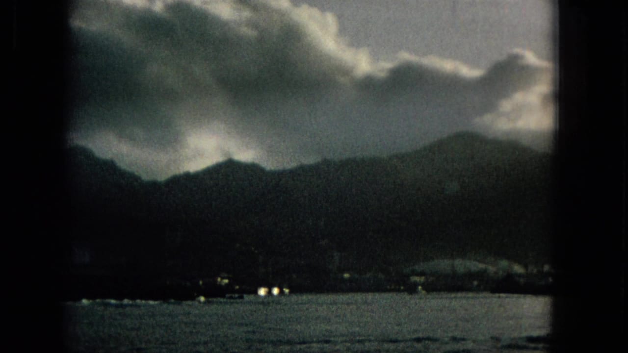 A dark coastal mountain view under heavy clouds appears across the water, with small shoreline lights or structures near the waterline.