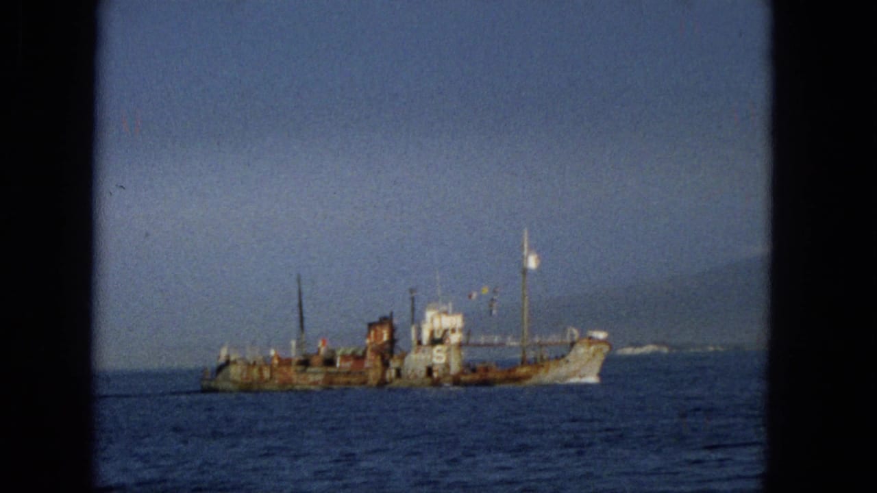 1965 Hawaii 8mm frame showing a weathered vessel marked with a large number 6 on calm ocean water, seen through dark film or window borders.