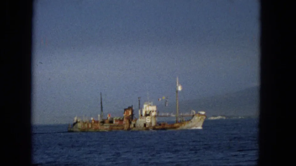 1965 Hawaii 8mm frame showing a weathered vessel marked with a large number 6 on calm ocean water, seen through dark film or window borders.
