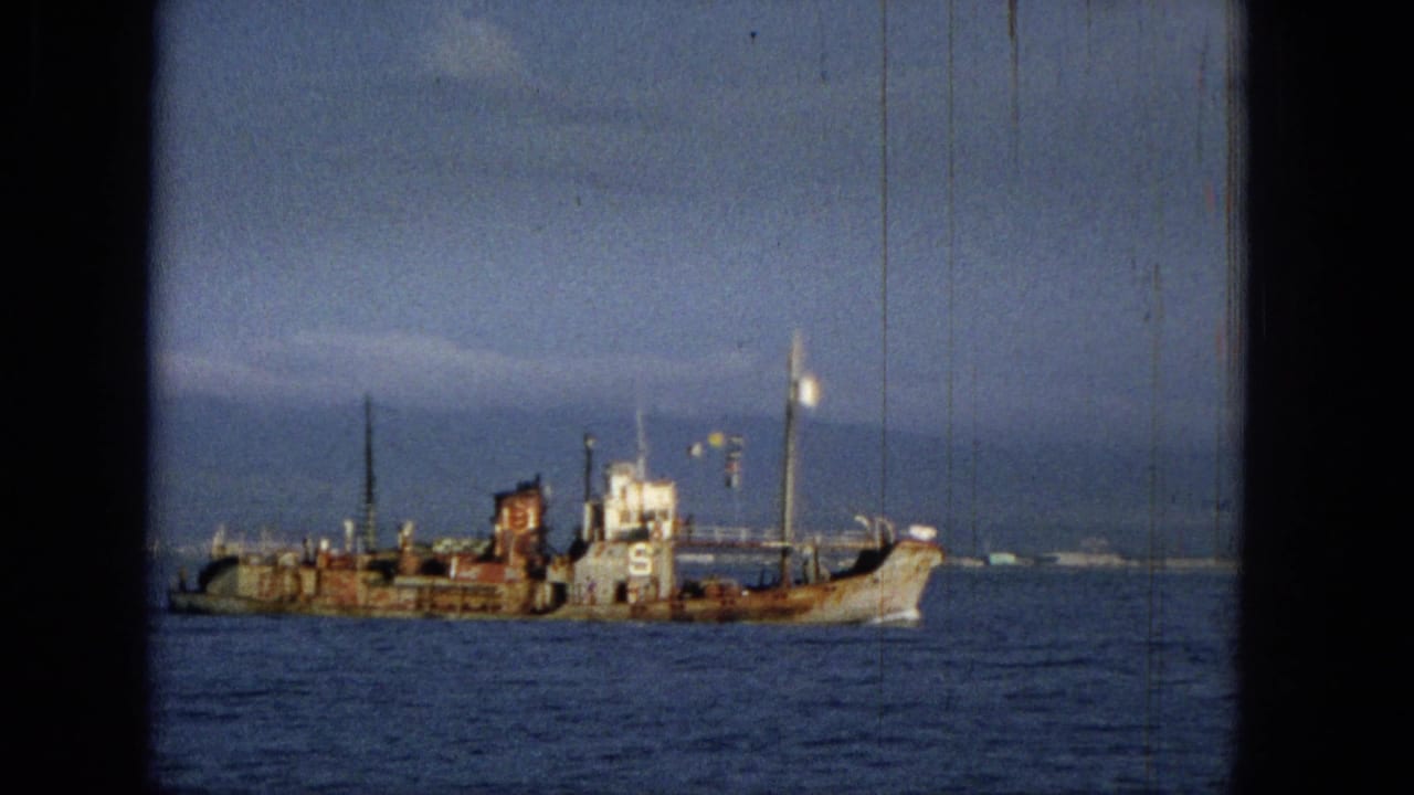 1965 Hawaii 8mm frame showing a weathered small ship or workboat on calm blue water with distant land on the horizon.