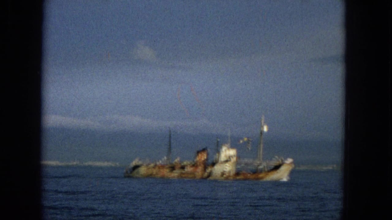 Small weathered ship farther across the water with hazy land behind it.