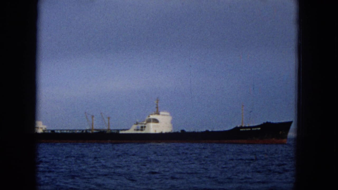 Side view of a long ship crossing calm water with dark film borders visible.