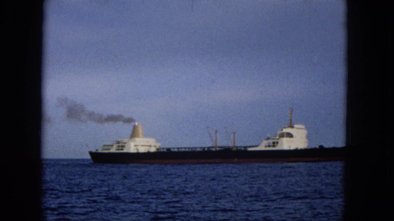 1965 Hawaii 8mm frame showing a dark-hulled vessel on blue water, with white structures and smoke trailing behind its funnel.