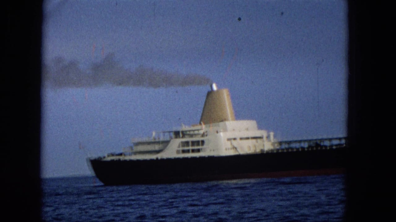 Tight 1965 Hawaii home-movie view of the cargo ship's white superstructure and funnel, with dark smoke drifting across the sky above the ocean.