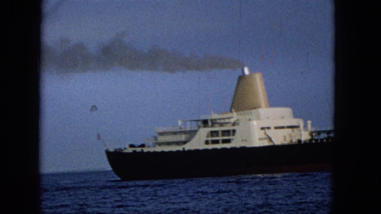 Large dark-hulled tanker on blue ocean with a white superstructure and smoking funnel.