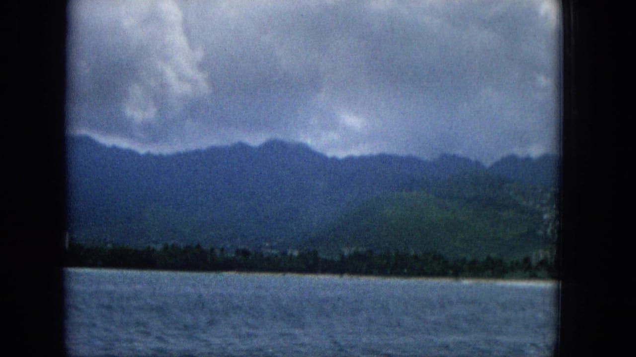 Wide water view toward a low shoreline, mountains, and heavy clouds.
