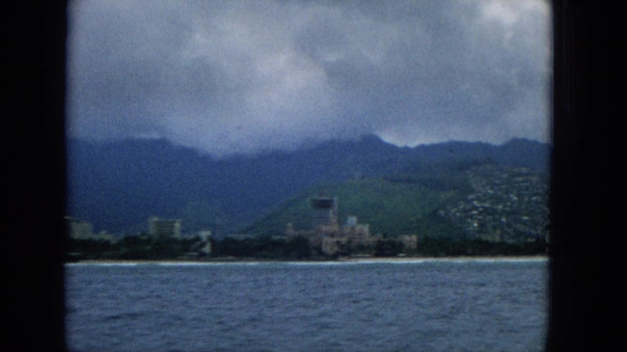 Waterfront buildings and hillside houses beneath dark mountain clouds.