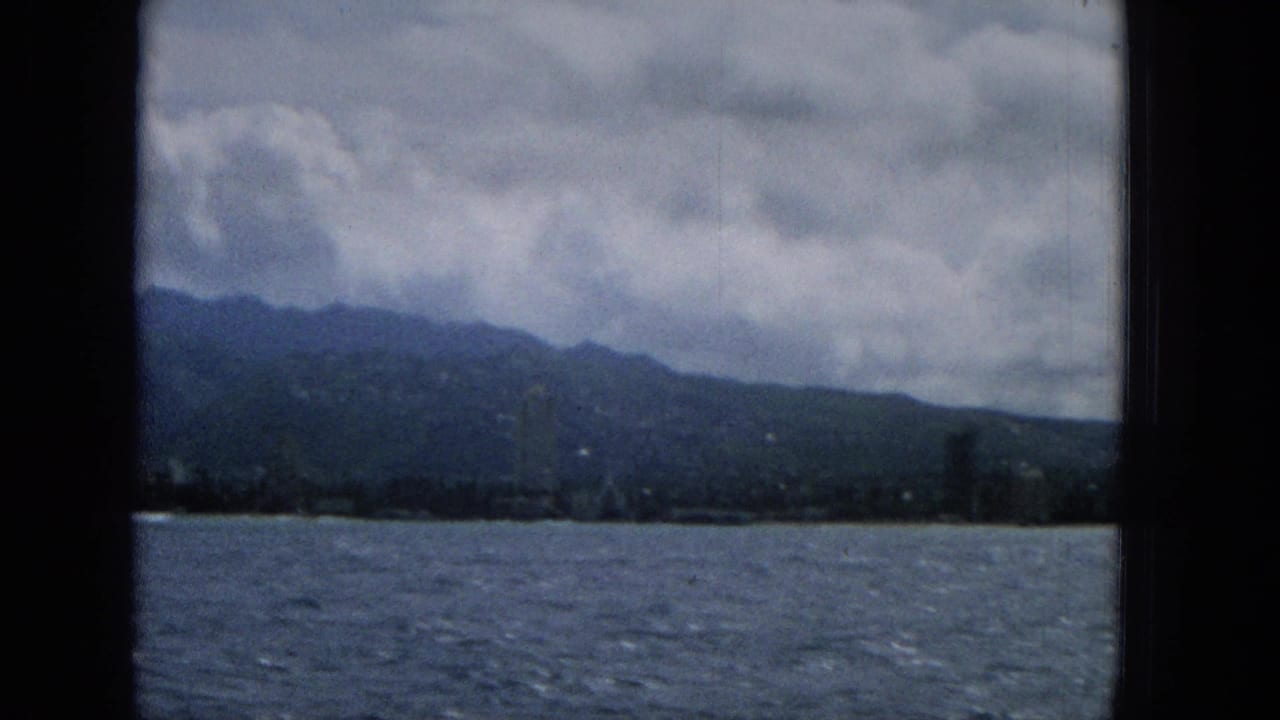 A Hawaii waterfront skyline and mountain backdrop appear across choppy water, with dark vertical window framing and heavy cloud cover.