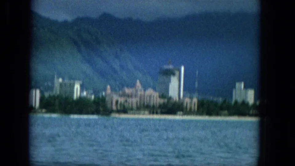 The final frame shows a Hawaii coastal cityscape with pale beachfront structures, a high-rise tower, choppy water, and mountain slopes divided by dark window framing.