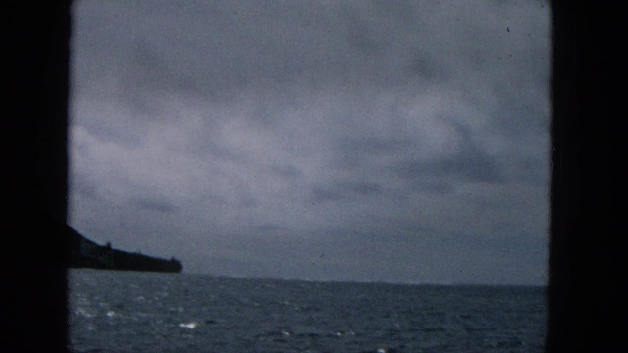 1965 Super 8 frame from a moving boat showing open ocean, low clouds, and a dark coastal point at the left edge, likely off Molokai based on clip metadata.