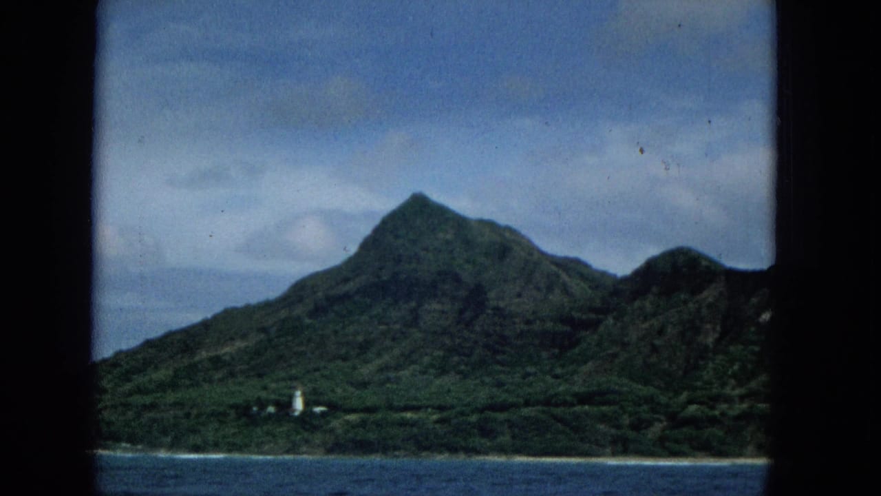 Mountainous green shoreline viewed across the ocean under a cloudy sky.