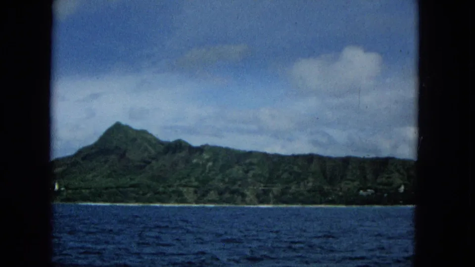 1965 Hawaii travel footage shows a prominent green peak and ridgeline on Molokai, filmed from a moving boat across the ocean.