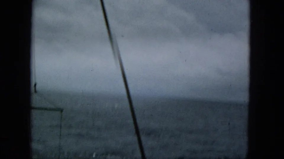 The view shifts toward open water, with a low ocean horizon, gray cloud cover, and a dark diagonal line of boat rigging crossing the 8mm frame.