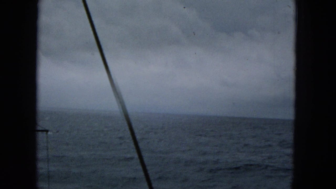 1965 Super 8 view of choppy ocean water through dark boat window framing and rigging, with a low overcast horizon.