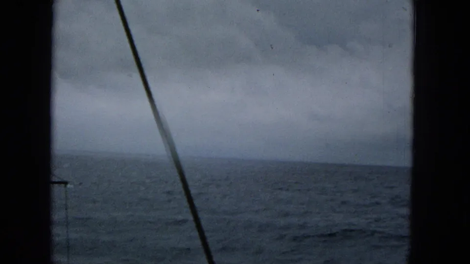 1965 Super 8 view of choppy ocean water through dark boat window framing and rigging, with a low overcast horizon.