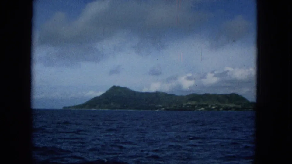 1965 Super 8 view toward Molokai from a boat, with blue ocean in the foreground, green slopes on the horizon, and dark window framing at the sides.