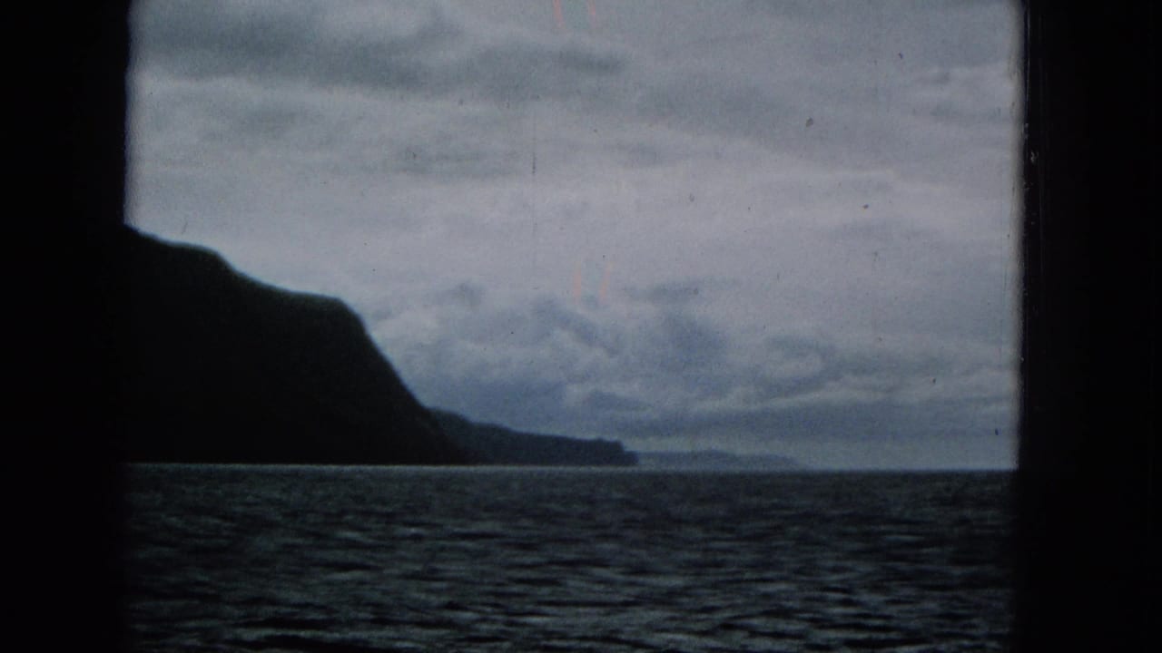 Dark coastal cliff silhouette above open water beneath an overcast sky.