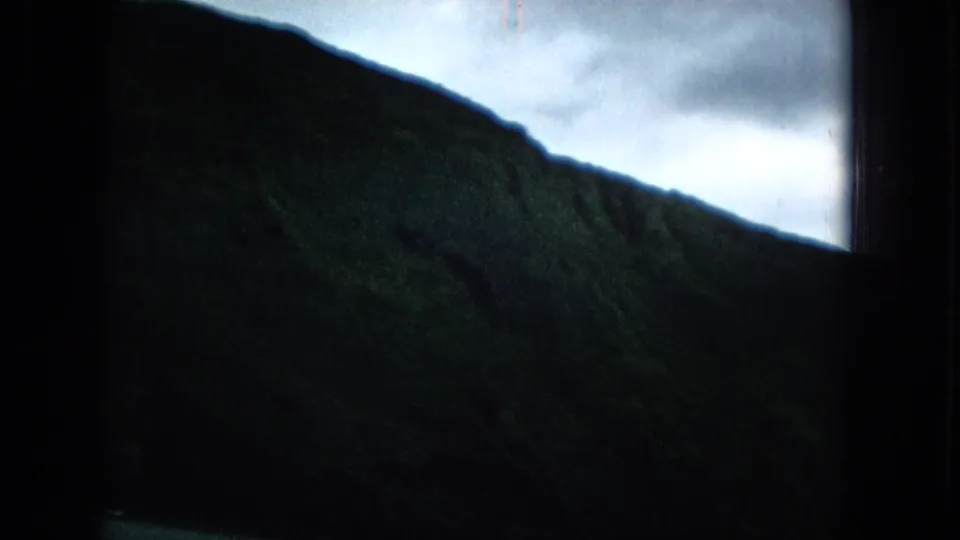 Green Molokai slope comes into clearer view under pale cloud cover, with the small-gauge film frame still heavily shadowed at the edges.
