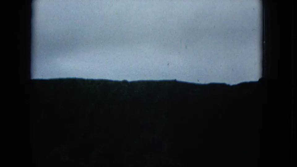 A dark, nearly silhouetted landscape band lies below a pale grey sky, with the 8mm frame showing grain, dust, and exposure falloff.