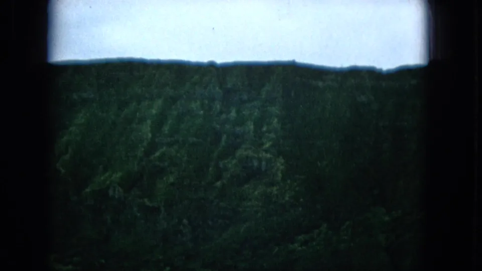 A green forested hillside appears beneath a bright pale sky in the final 1965 8mm frame, with dark borders and soft home-movie exposure.