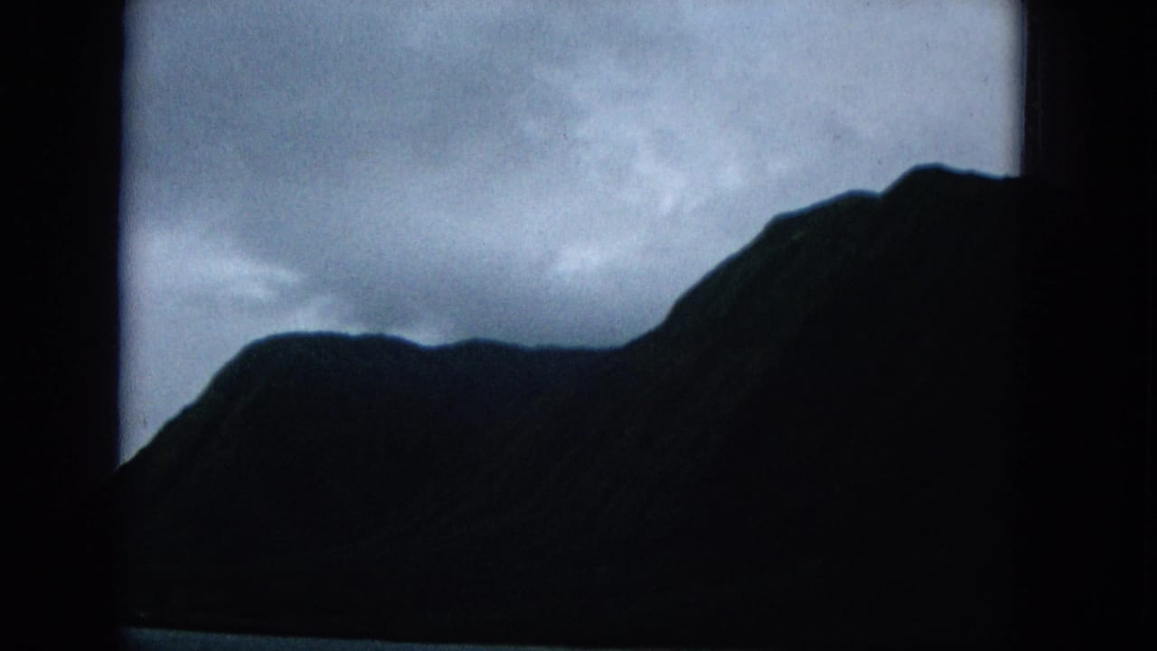 1965 Molokai coastal view with steep dark mountain forms under heavy cloud cover.