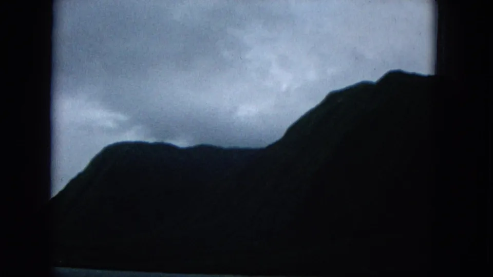 1965 Molokai coastal view with steep dark mountain forms under heavy cloud cover.