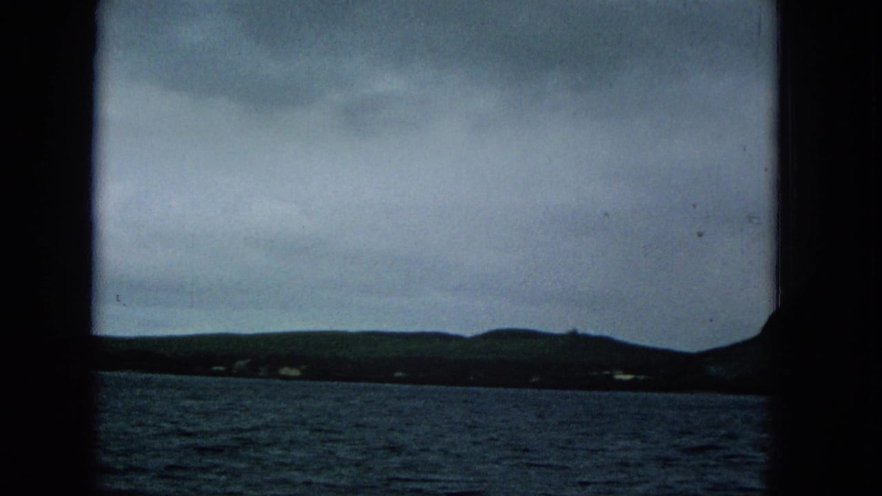 1965 Super 8 frame showing Molokai shoreline hills and scattered distant homes across choppy water from a boat viewpoint.