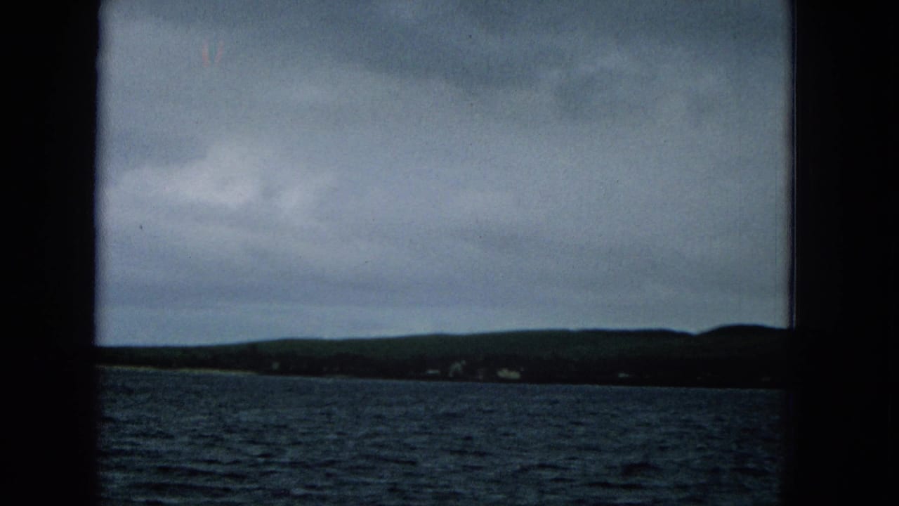 Cloudy coastal view with dark shoreline and water seen through film-frame borders.