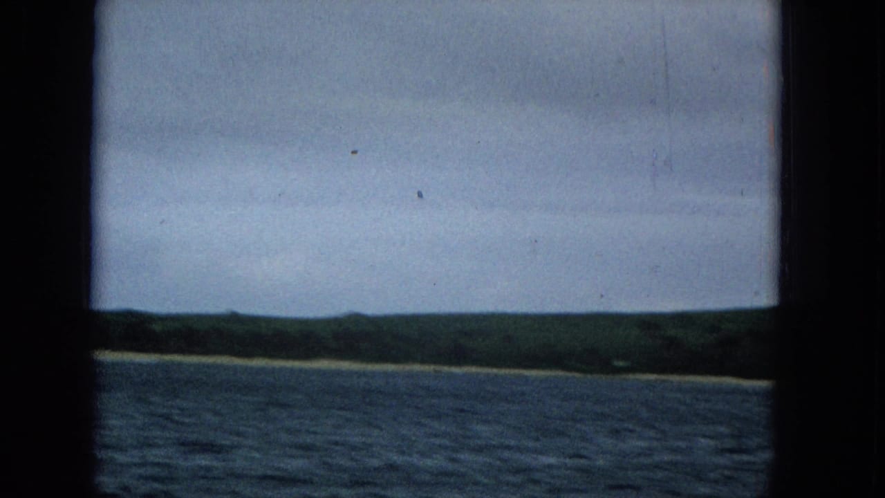 Distant coast with low hills and water, framed by dark film borders.