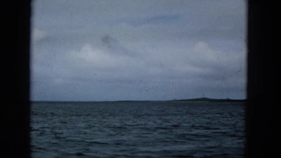 Super 8 view across choppy water toward a low island horizon, with soft grain and cloudy sky consistent with the 1965 home-movie metadata.