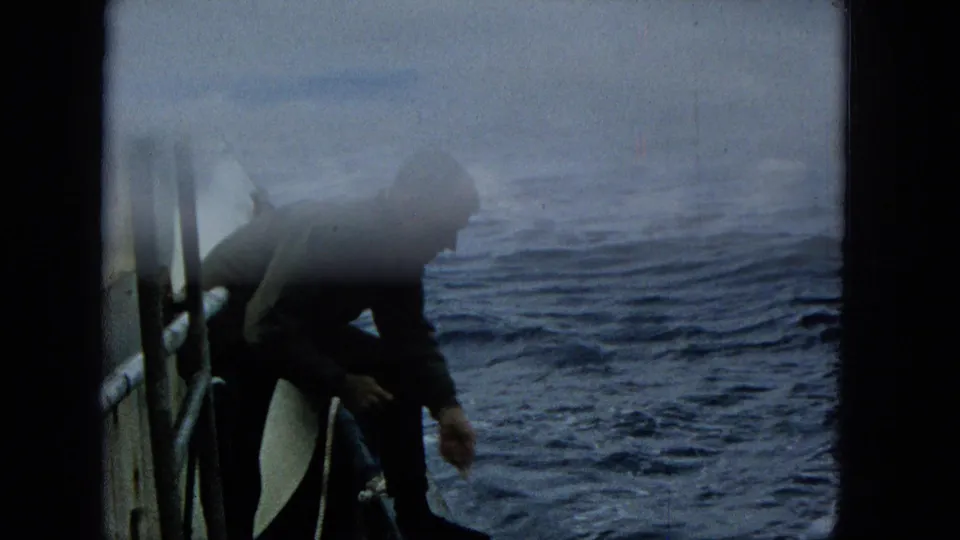 A man on a boat crouches beside the rail near the water, partially obscured by a pale exposure wash in the Super 8 frame.