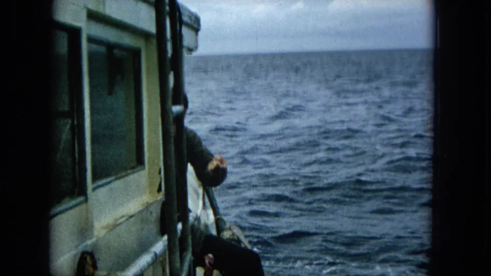 The camera frames the side of the small boat and the open ocean while the man remains partly visible near the edge, continuing the fishing action.