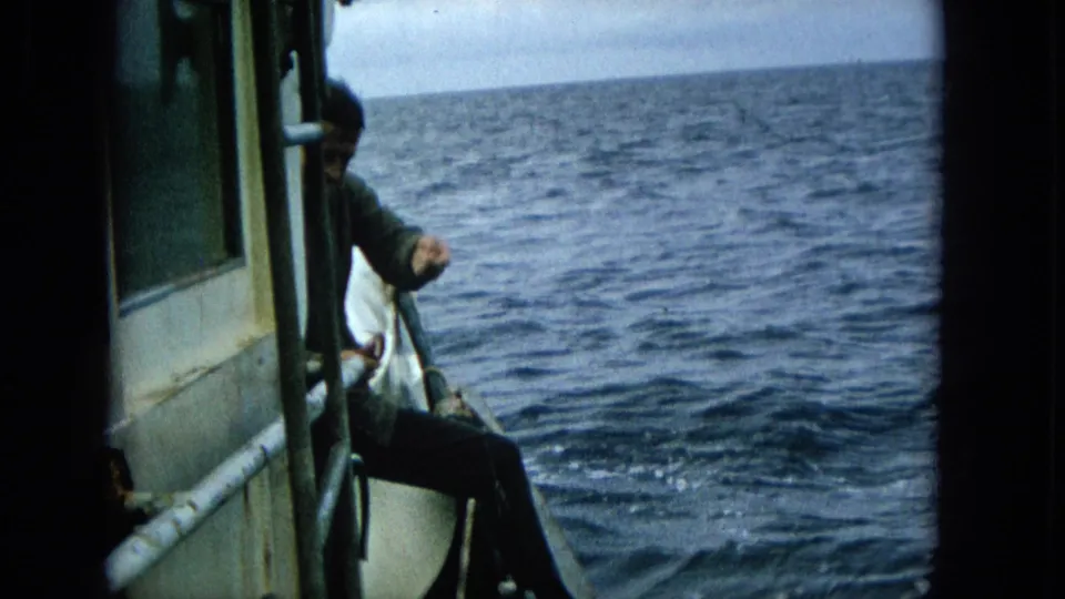 A man remains at the side of the small boat above the rippling open ocean, with the handheld camera staying close to the fishing action.