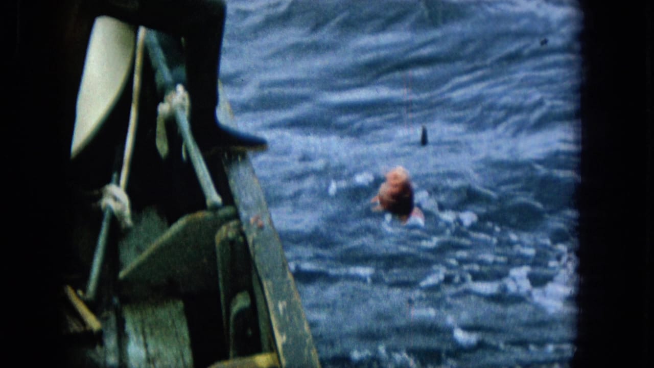 A bright red fish surfaces in choppy blue water next to the boat as fishing gear and the boat edge remain visible in the foreground.