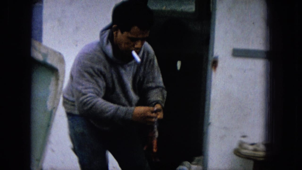 Man in a gray hoodie smoking while handling a fish near a boat or dock surface.