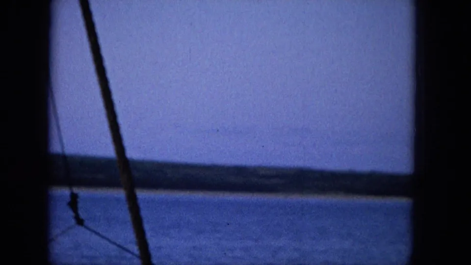 The vessel-side view includes calm blue water, a low shoreline, dark framing bars, and a diagonal rope or rigging line at the left edge.