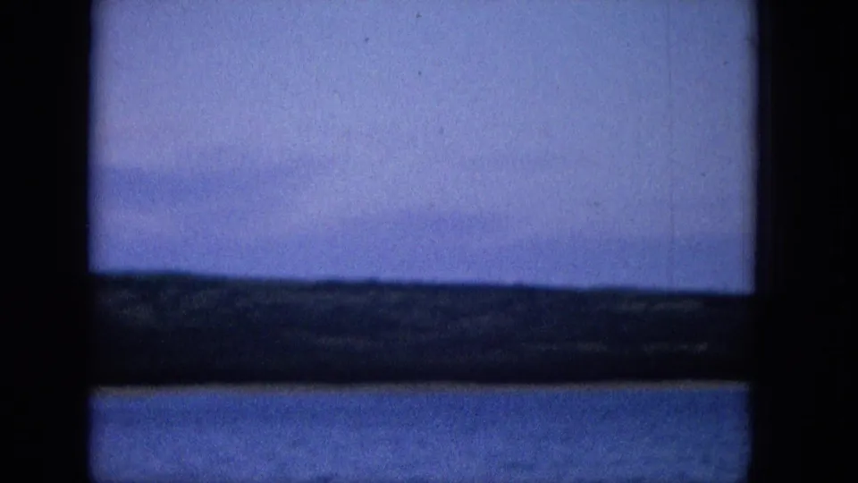 1965 Super 8 frame showing a quiet water view through a dark window frame, with a low shore, muted sky, and soft film exposure.
