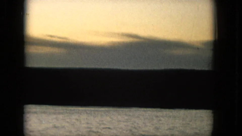 1965 Super 8 frame from supplied Molokai metadata showing layered clouds, a dark horizon line, and rippled water seen through a window-like opening.