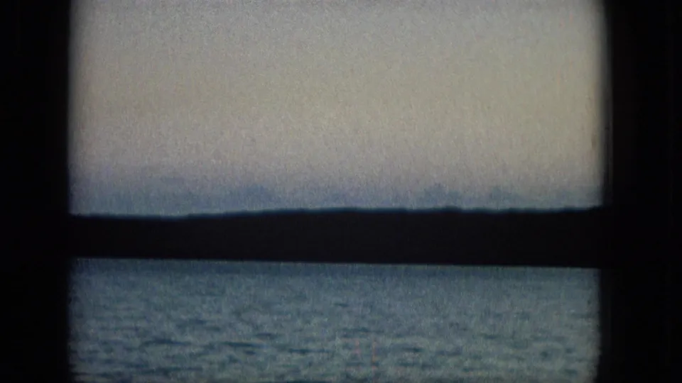 The final frame shows pale sky over a low distant horizon and calm water, divided by a dark window frame in a quiet coastal home-movie view.