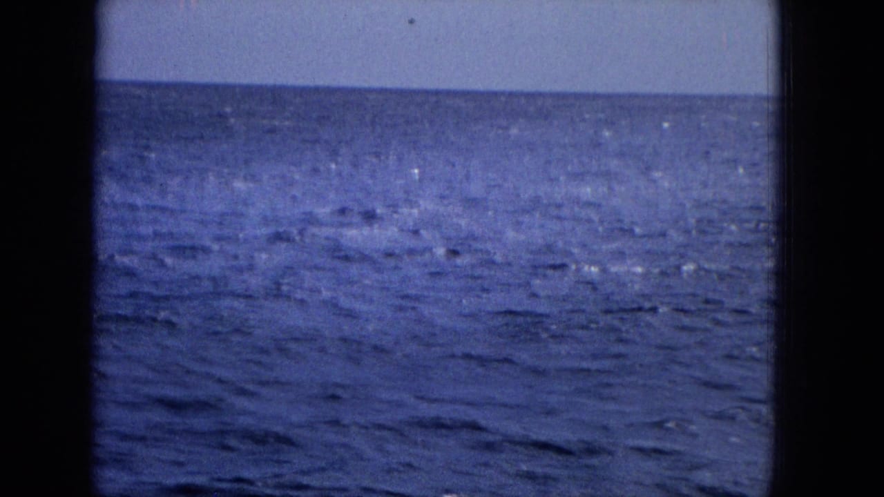 Final 1965 home-movie frame of open ocean near Molokai, with the fin mostly submerged or out of view and only water texture visible.