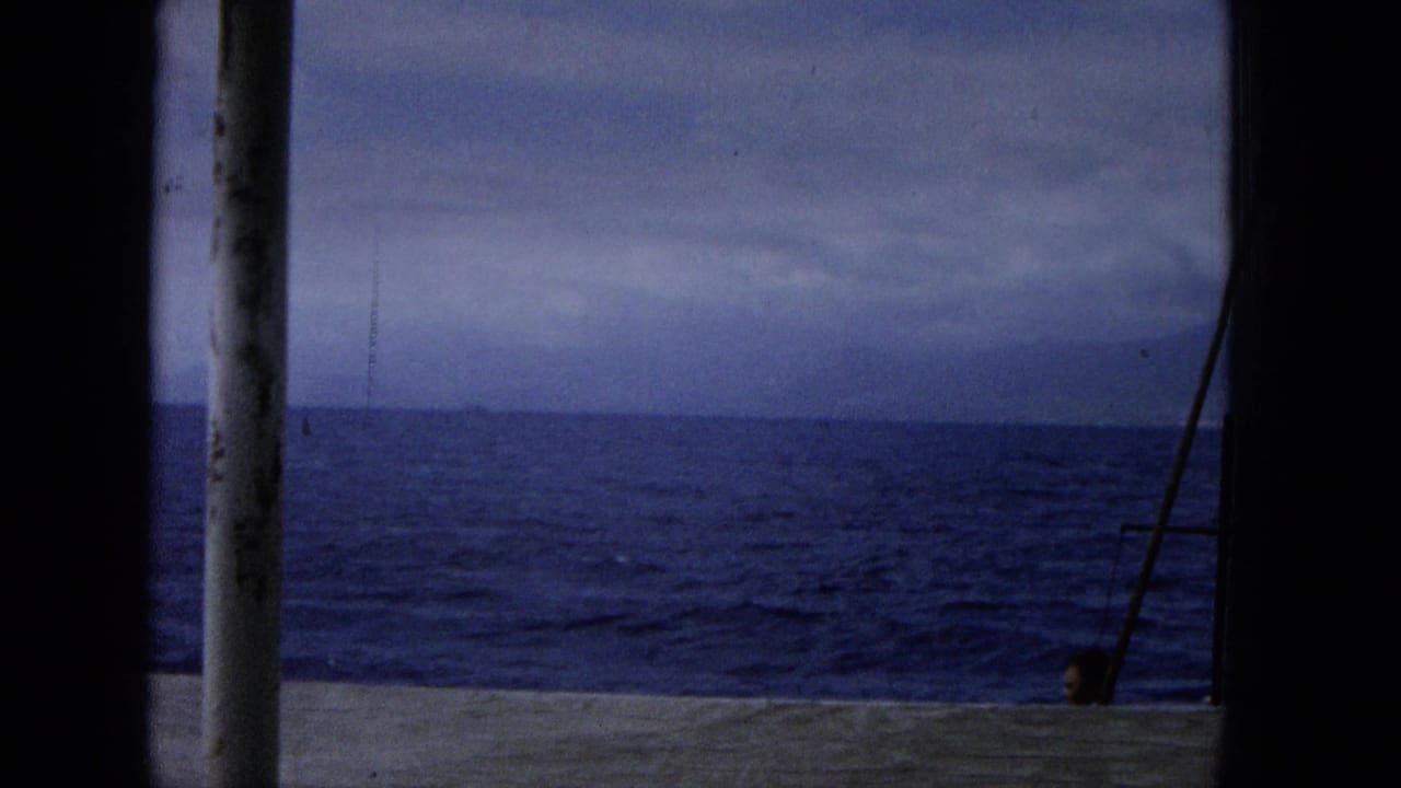 Boat deck rail, vertical post, open ocean, and cloudy horizon.