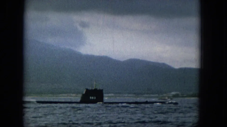 A dark submarine crosses the lower part of the 8mm frame, seen through heavy dark borders with choppy water in front and muted mountains behind.