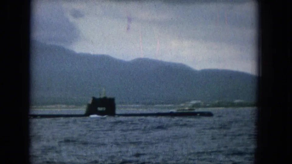 Final frame of the short clip shows the surfaced submarine extending across the water, with a dark conning tower, muted mountains, and cloudy sky in soft 8mm color.