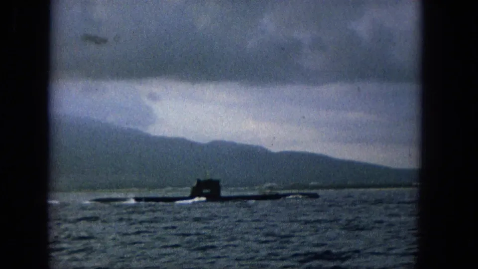 The submarine continues across the ocean in a soft, grainy 1965 frame, with low waves, distant hills, and cloudy sky forming the background.