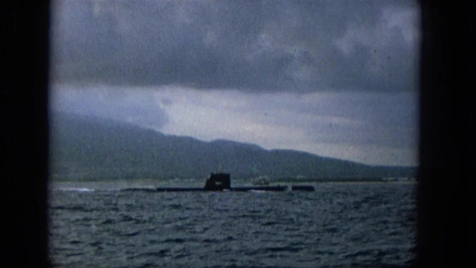 Final frame shows the submarine lower and more distant on Molokai waters, with dark foreground borders, textured sea, muted hills, and an overcast sky.