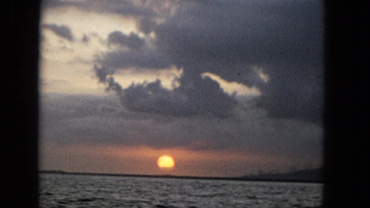 Low sun glows through clouds above a dark ocean horizon, bordered by a vertical frame bar.