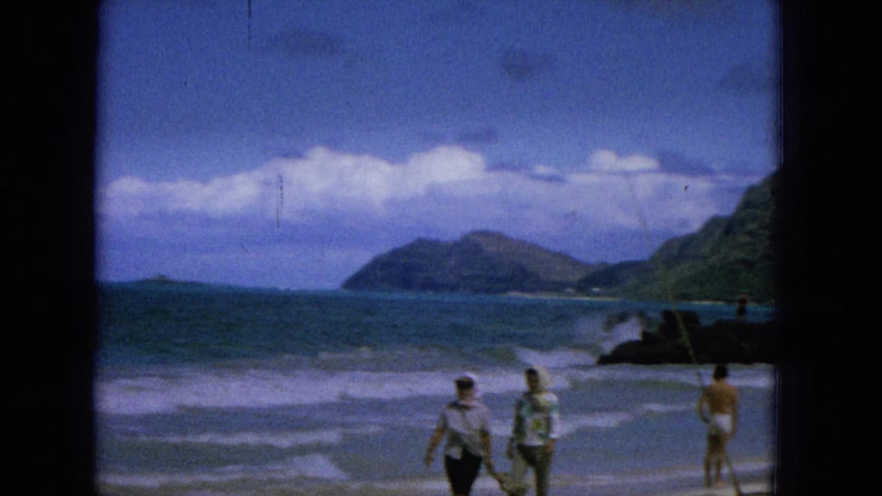 Two people walk near the surf as another person stands farther down the beach.