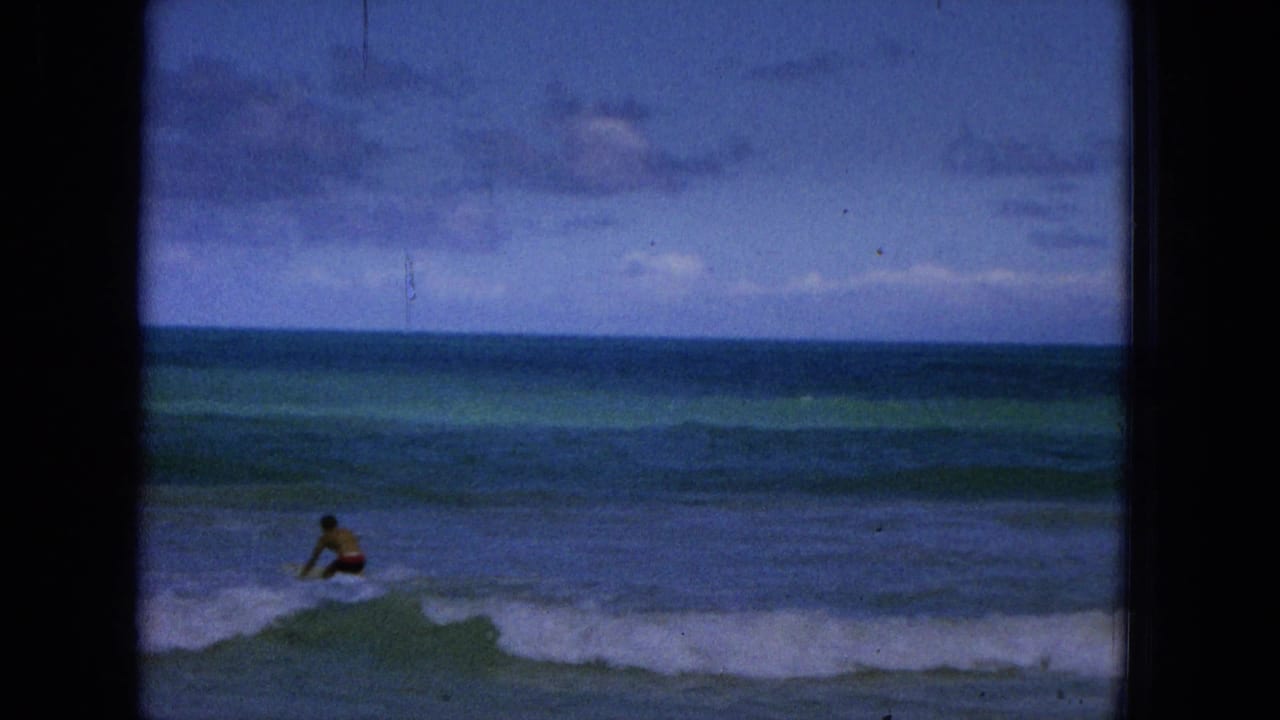 Distant person in the surf paddling or wading through small waves under a cloudy sky.