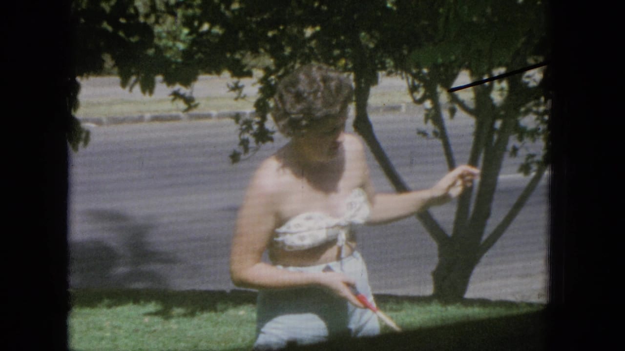 Woman stands under leafy trees holding a badminton racket in a yard.