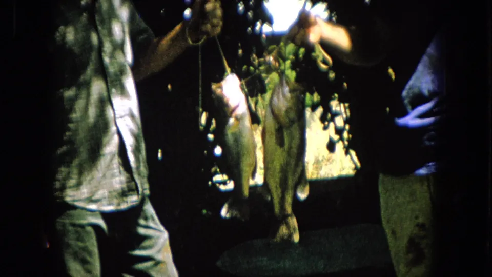 The catch remains centered in frame, with two fish hanging from strings between partially visible adults in a high-contrast backyard scene.